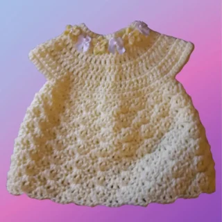 Handmade crochet shell stitch baby dress with decorative flowers sewn onto the neckline