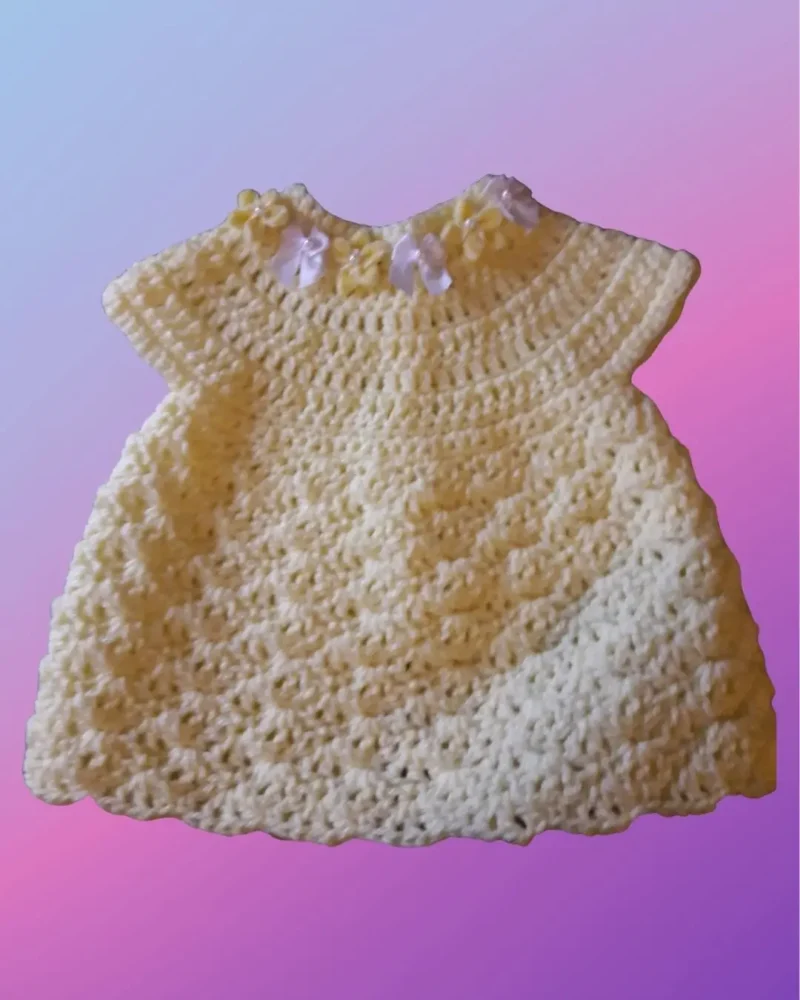 Handmade crochet shell stitch baby dress with decorative flowers sewn onto the neckline